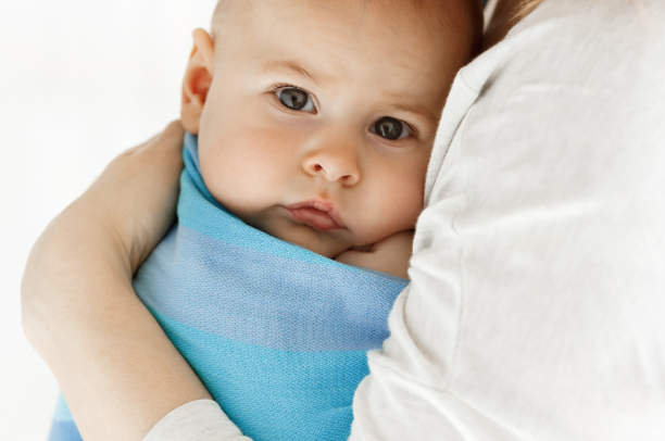 Close up of sweet little baby boy looking at camera with his big grey eyes. Mom snuggle her child with tenderness and love. Family concept