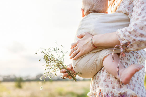 Little baby boy and his mother walking in the fields. Mother is holding and tickling her baby, babywearing in sling